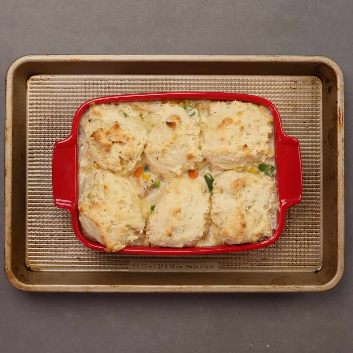 a baked chicken casserole with biscuit topping in a red baking dish.