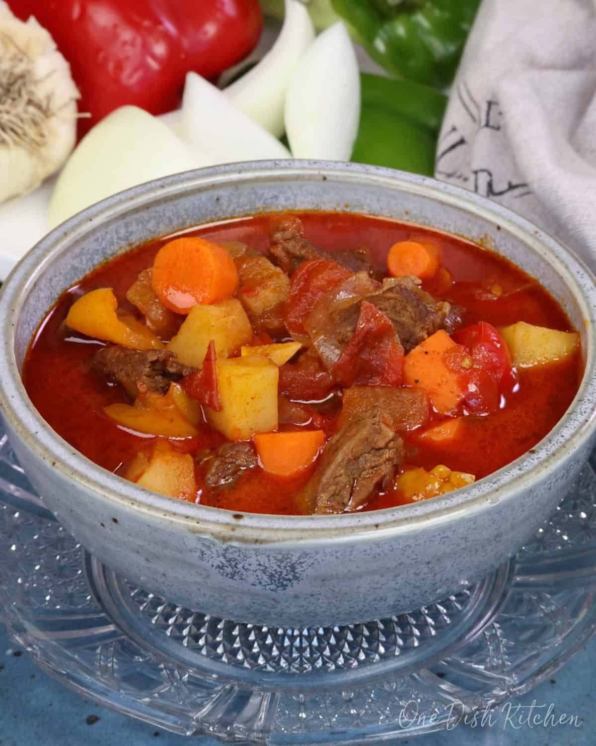 a blue bowl filled with hungarian goulash next to fresh vegetables.