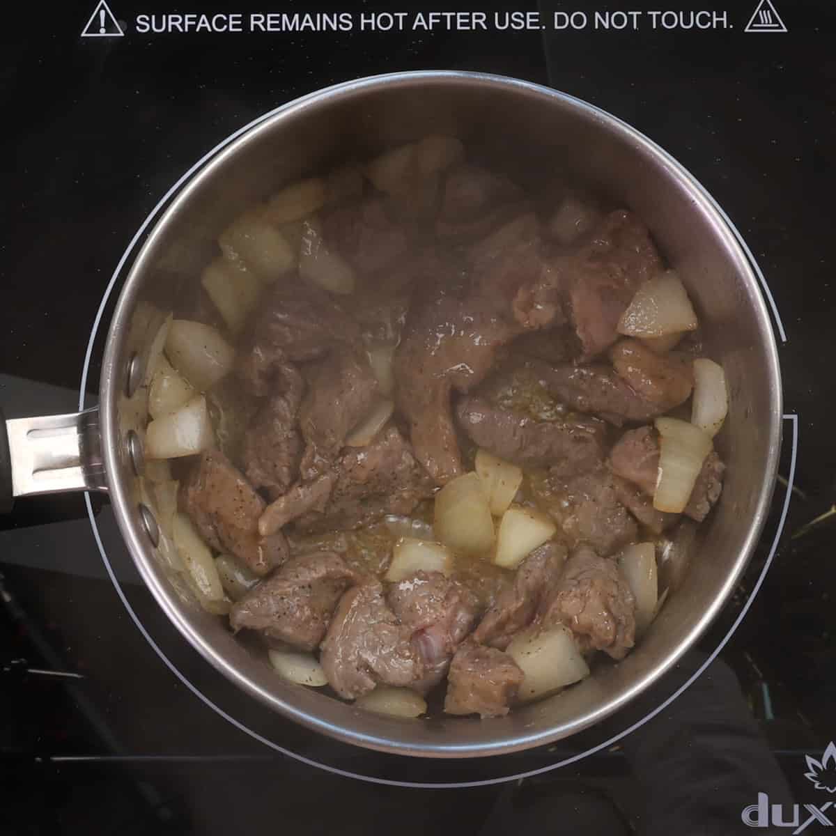 beef and onions cooking in a small pot.