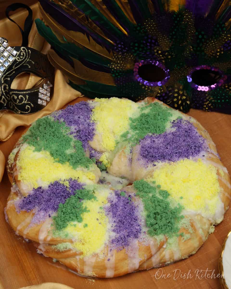 a small traditional king cake on a table next to two mardi gras masks.