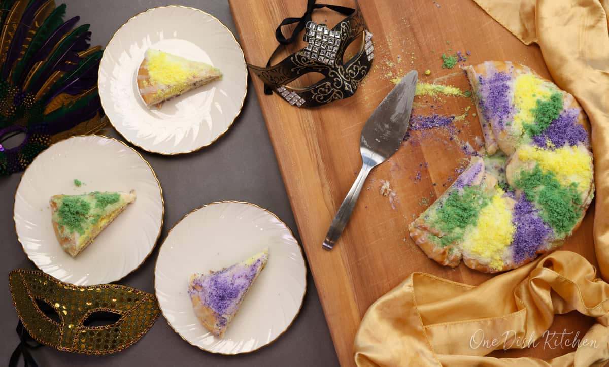 a small king cake cut into pieces with three slices of king cake on three plates.