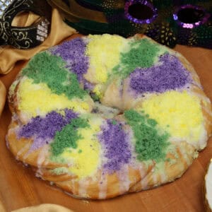 a small traditional king cake on a table next to two mardi gras masks.