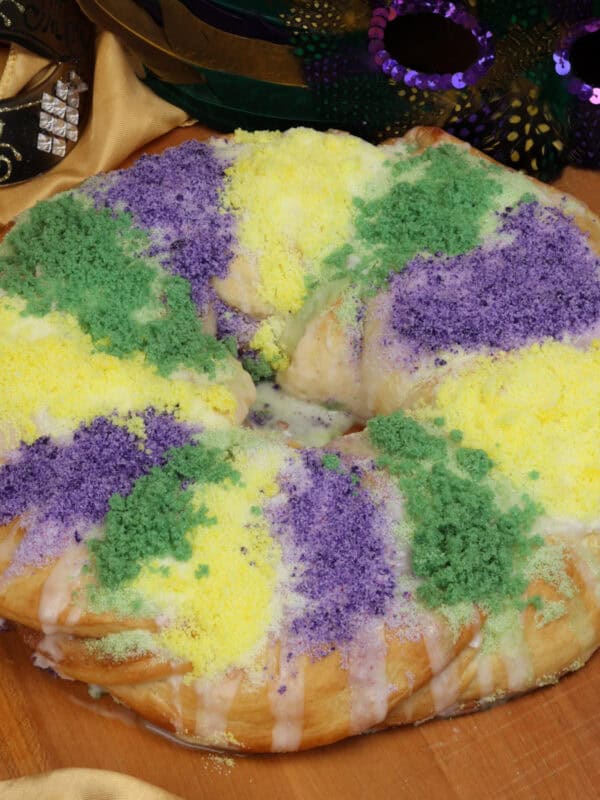 a small traditional king cake on a table next to two mardi gras masks.