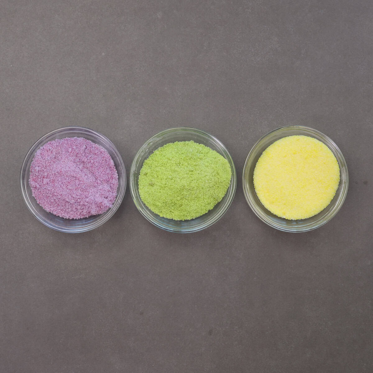 three bowls of colored sugar: purple, green and gold.