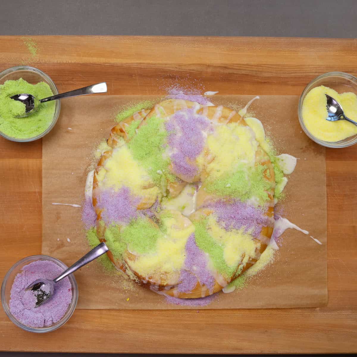 a king cake with bowls of colored sugar around the cake.