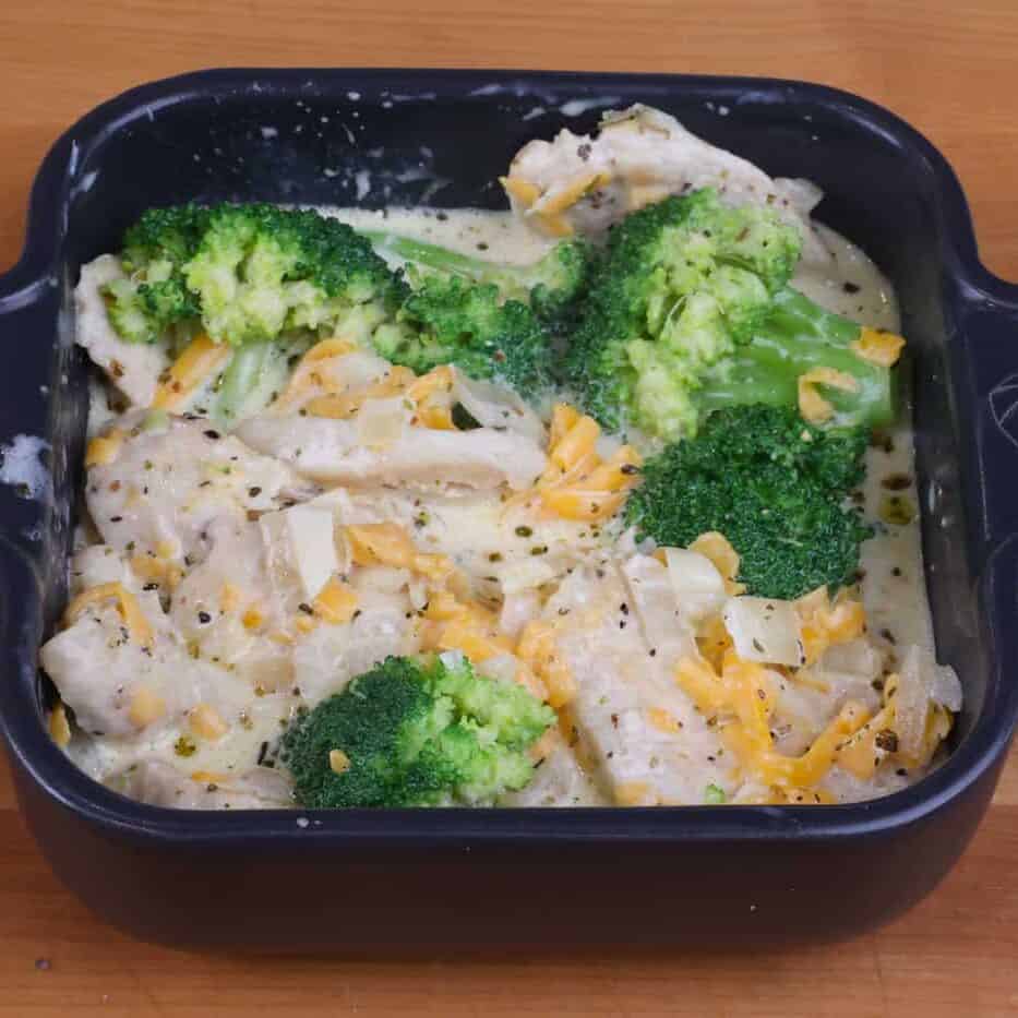 uncooked chicken divan in a small black square baking dish.