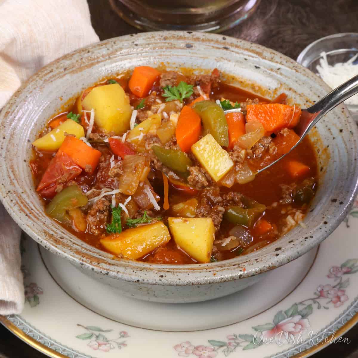 a bowl of hamburger soup with a spoon on the side.