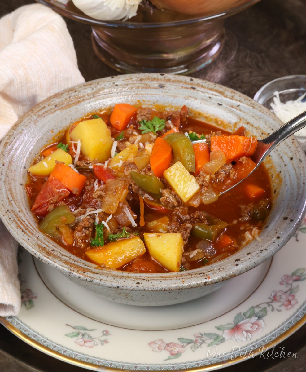 a bowl of hamburger soup with a spoon on the side.