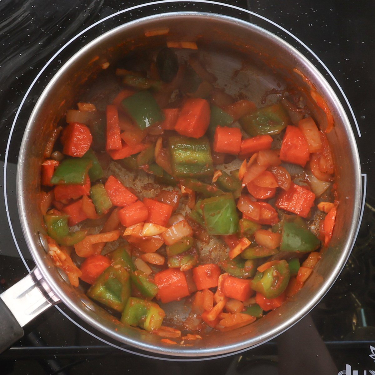 onions, carrots, bell peppers, and tomato paste cooking in a pot.