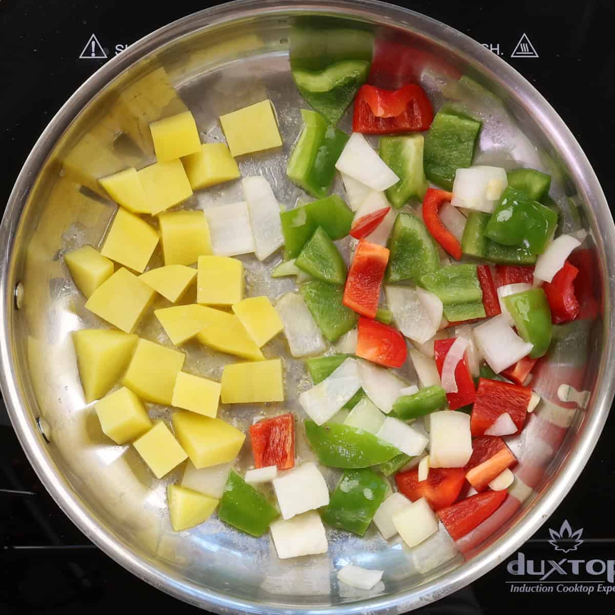 diced potatoes on one side of a skillet and onions and bell peppers on the other side.