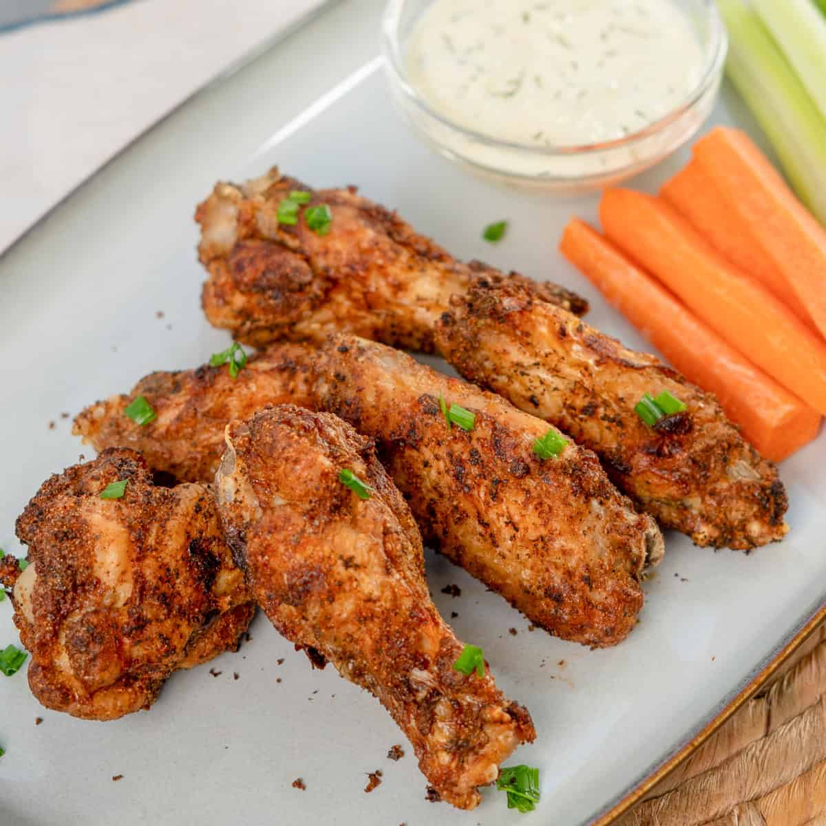 chicken wings on a blue plate next to ranch dressing, carrot sticks and celery sticks.