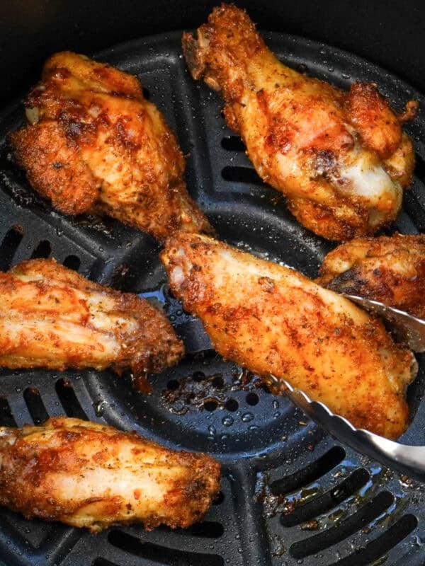 tongs lifting a chicken wing out of an air fryer.