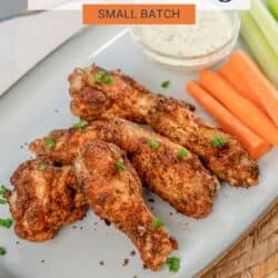 chicken wings on a blue plate next to ranch dressing, carrot sticks and celery sticks.