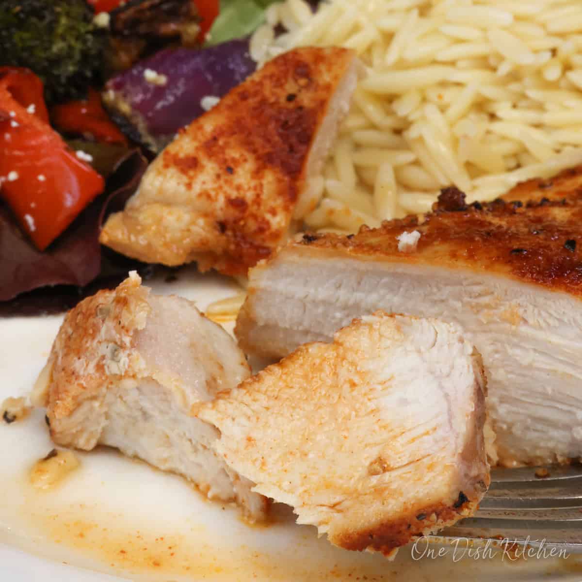 cooked chicken on a plate slice with a fork on the side.