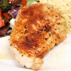 a baked chicken breast on a white plate next to salad and cooked orzo.