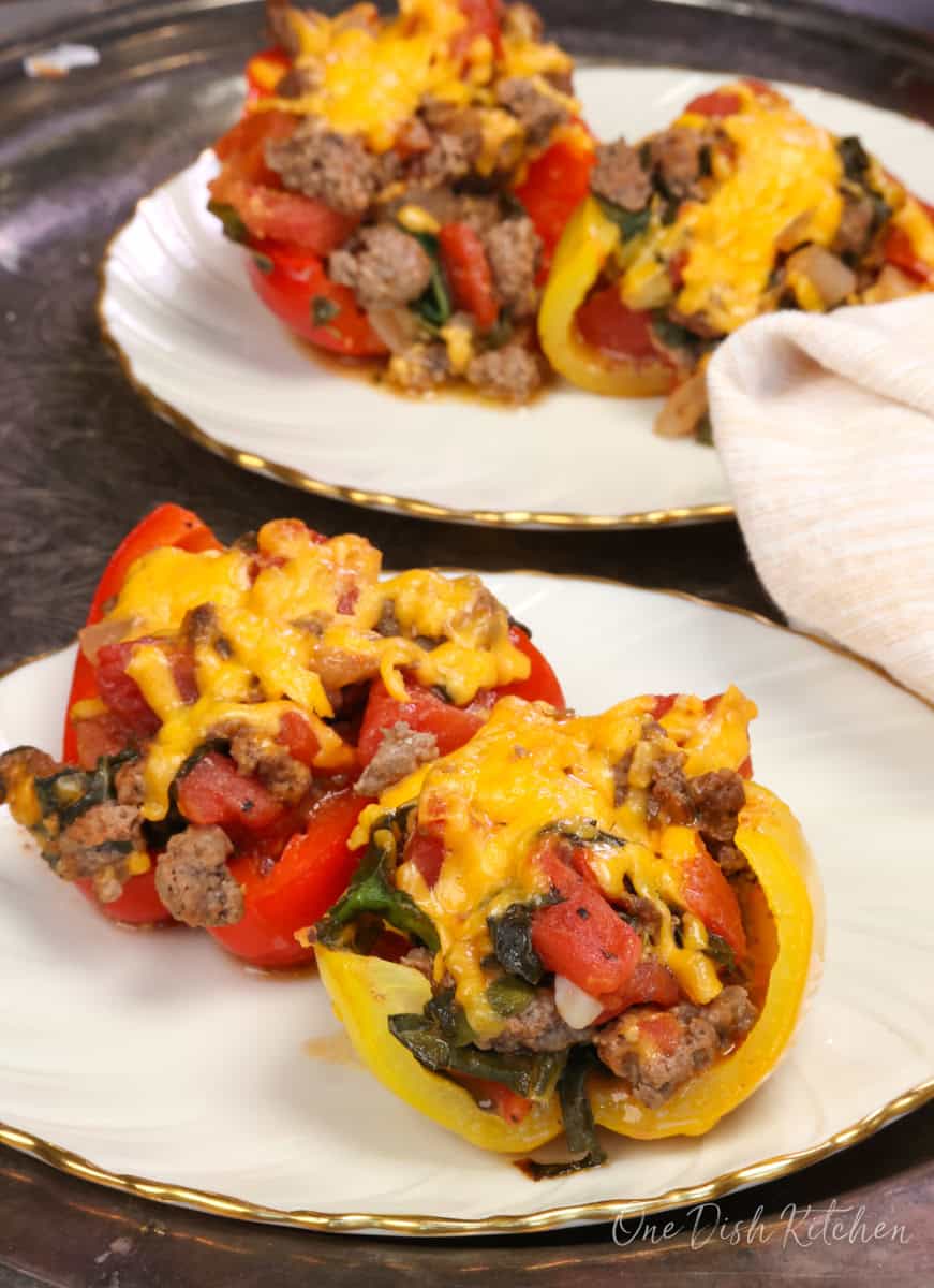 four stuffed pepper halves filled with ground beef and cheese on two plates.