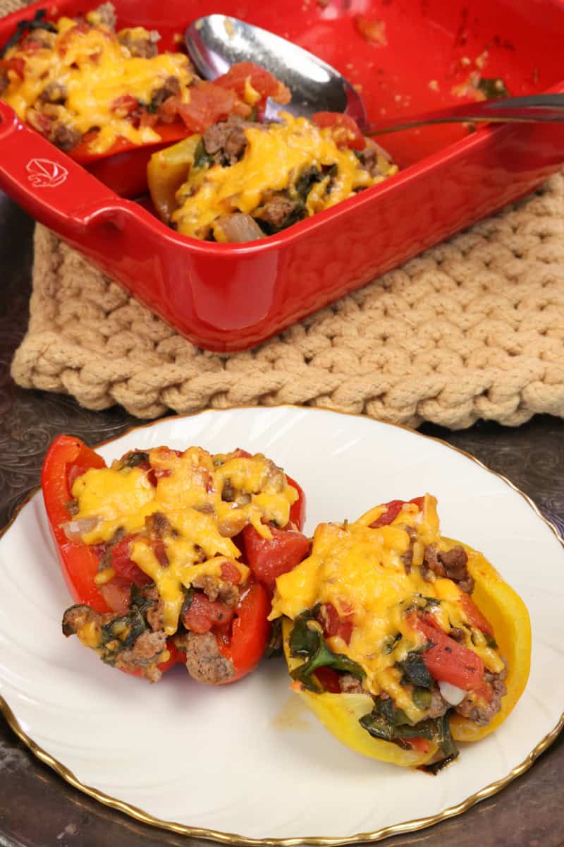 two stuffed bell peppers on a plate with two remaining peppers in a baking dish.