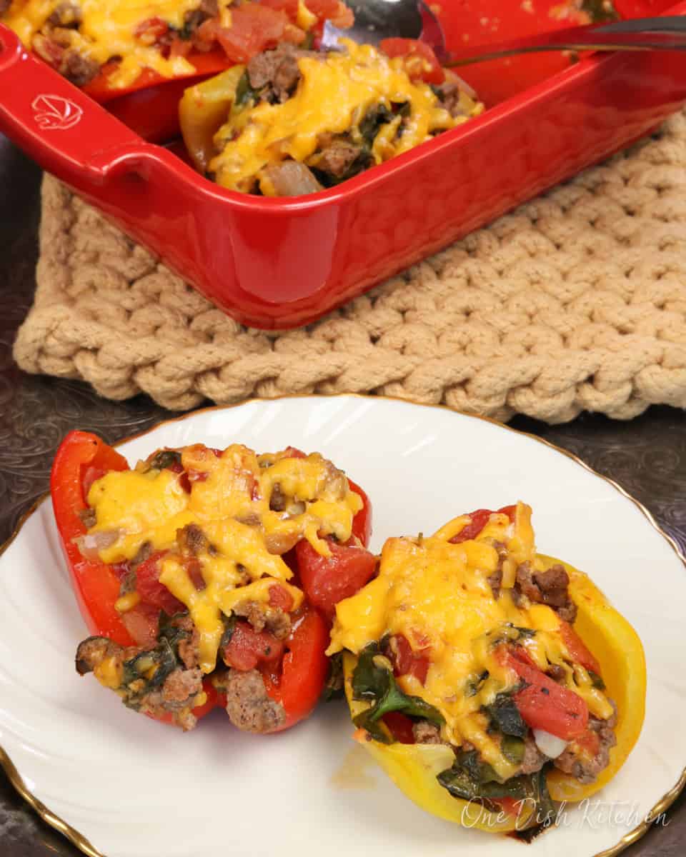two stuffed peppers on a plate with two remaining stuffed peppers in a red baking dish.
