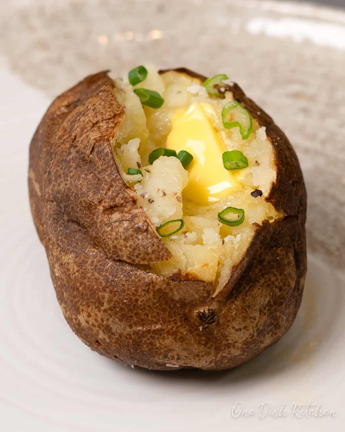 a single baked potato on a white plate topped with butter.
