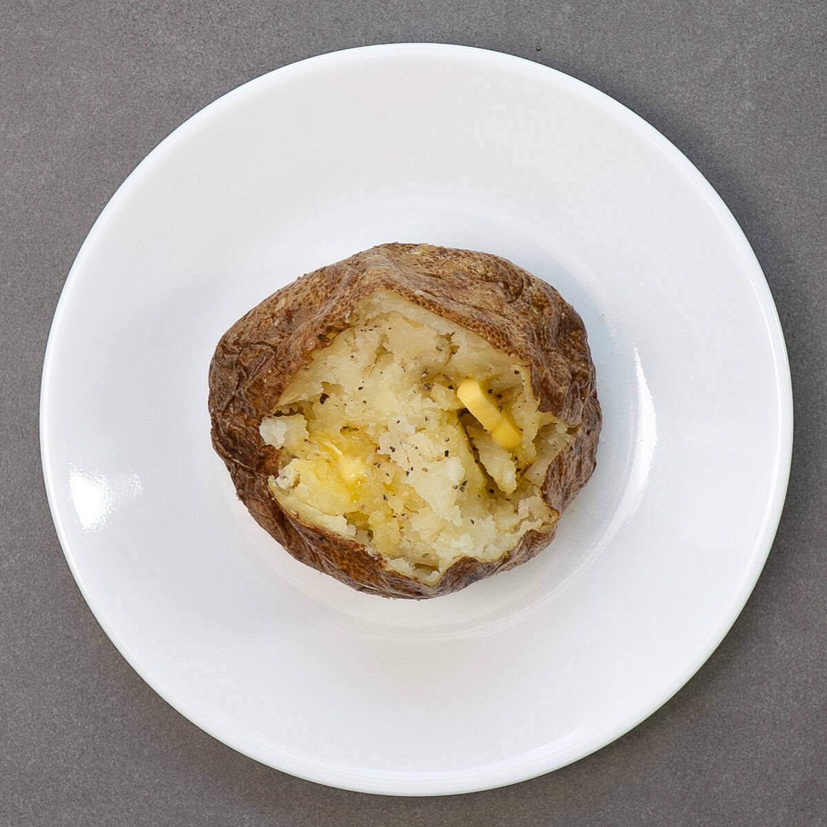 a baked potato with butter on a white plate.