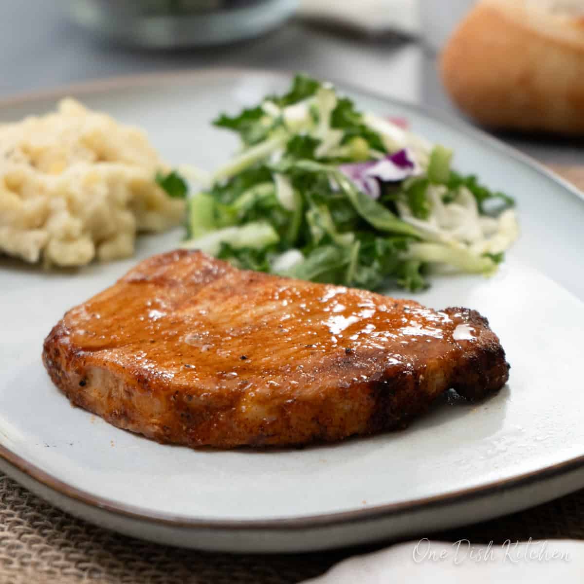 a cooked pork chop on a grey plate with a salad and mashed potatoes.