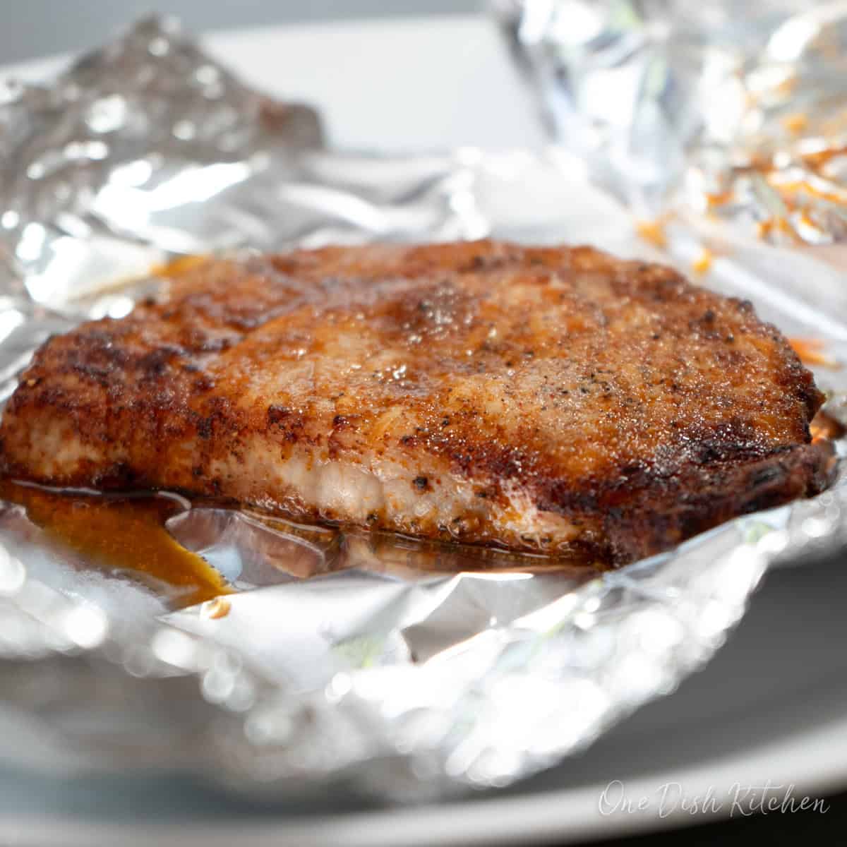 a boneless pork chop resting on foil on a plate.