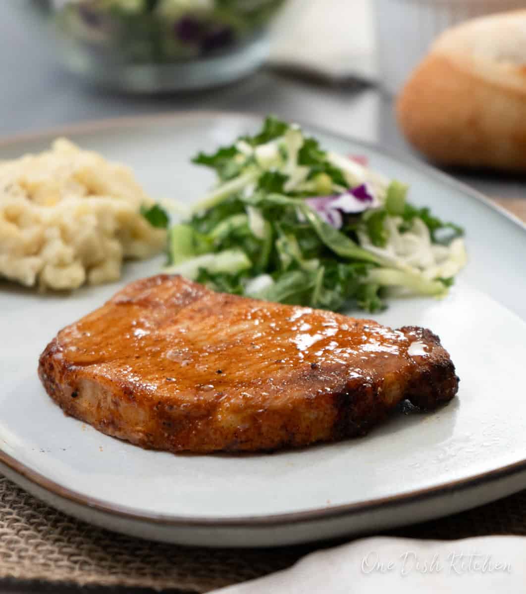 a cooked pork chop on a grey plate with a salad and mashed potatoes.