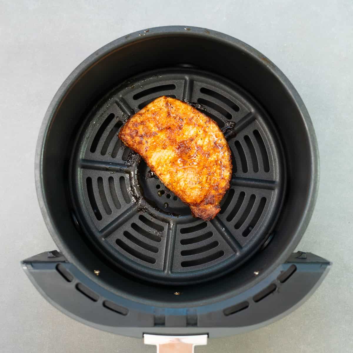 a cooked pork chop in an air fryer basket.