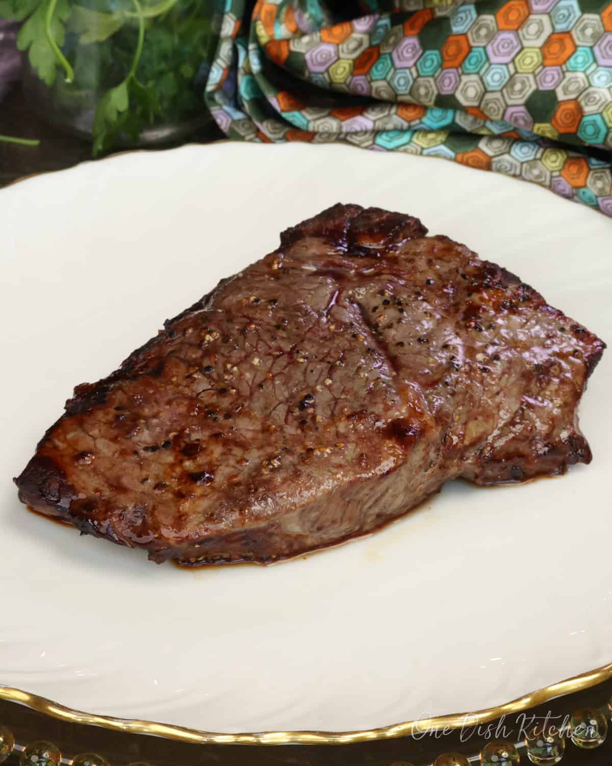 a sirloin steak on a white plate next to a bowl of parsley.