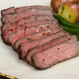 sirloin steak sliced on a plate next to green beans and potatoes.