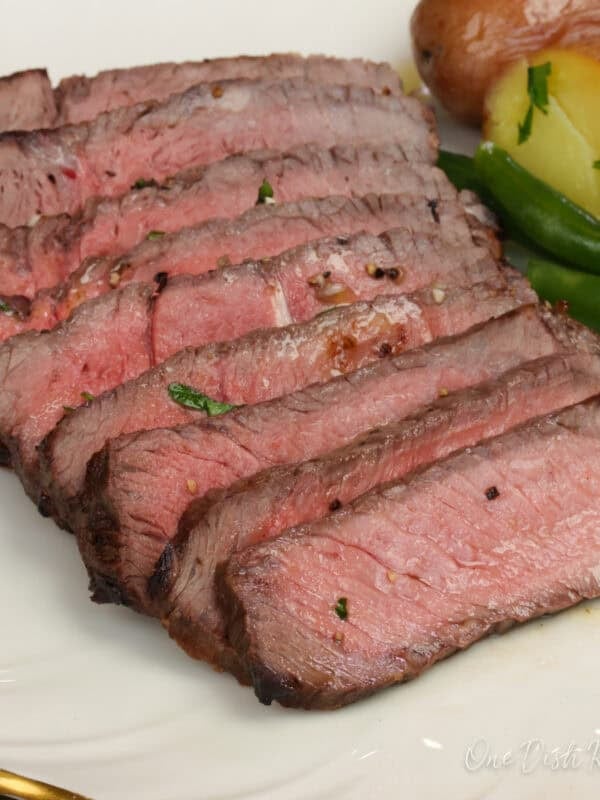 sirloin steak sliced on a plate next to green beans and potatoes.