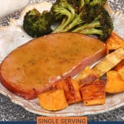 a baked ham steak on a white plate with roasted sweet potatoes and broccoli.