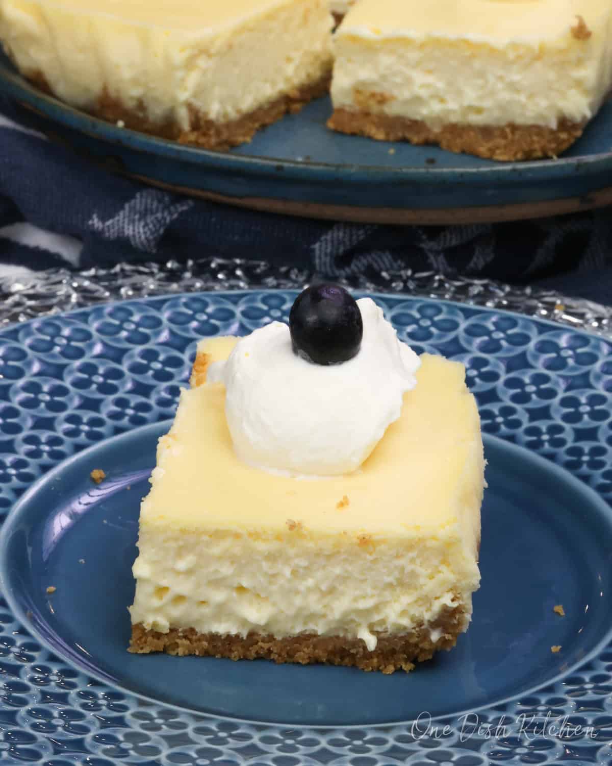 a slice of cheesecake on a blue plate with three other slices in the background.