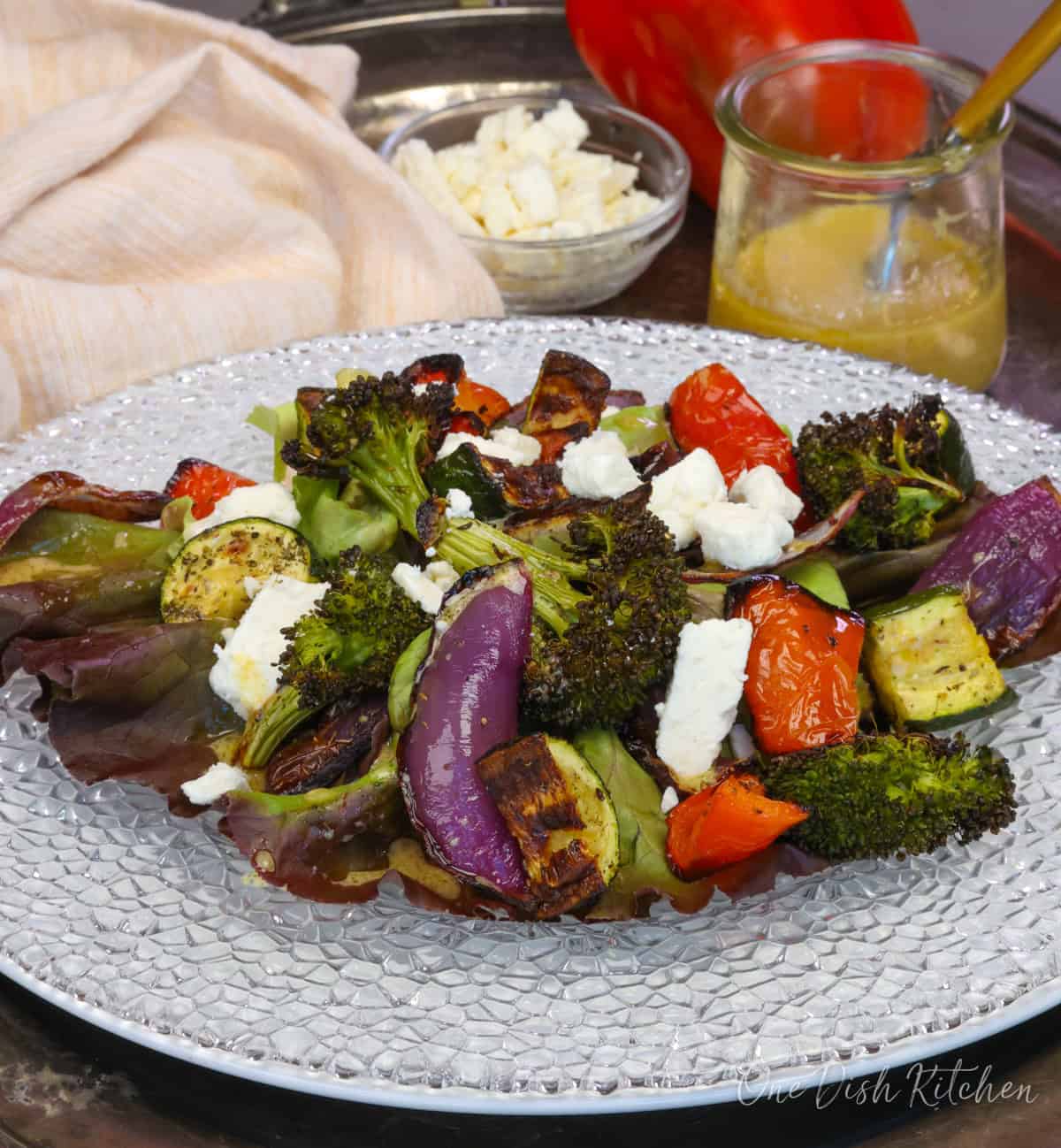 a roasted vegetable salad on a white plate topped with feta cheese and a vinaigrette.