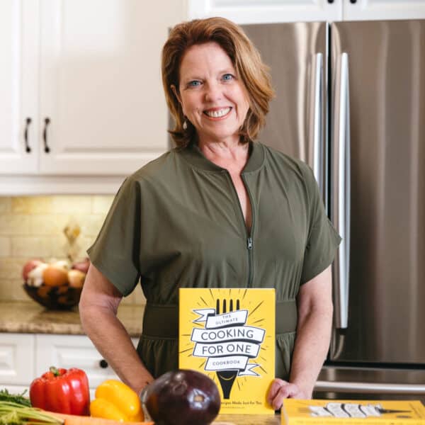 women in green dress standing and holding a cookbook.