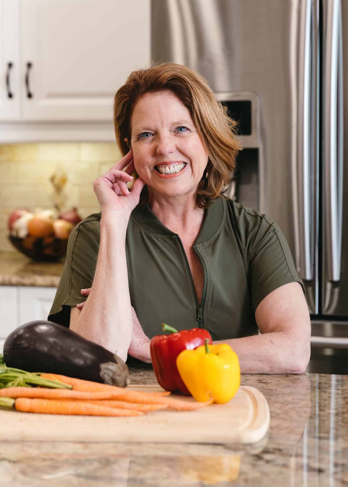 women in green dress sitting in kitchen with vegetables in front of her.