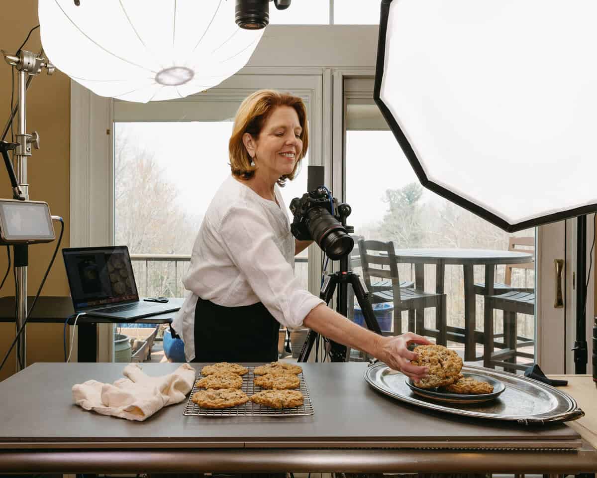 women in white shirt next to camera and holding a cookie.