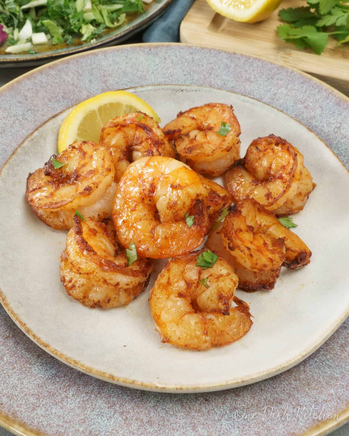 cooked shrimp on a grey plate next to a lemon wedge and a fresh salad.