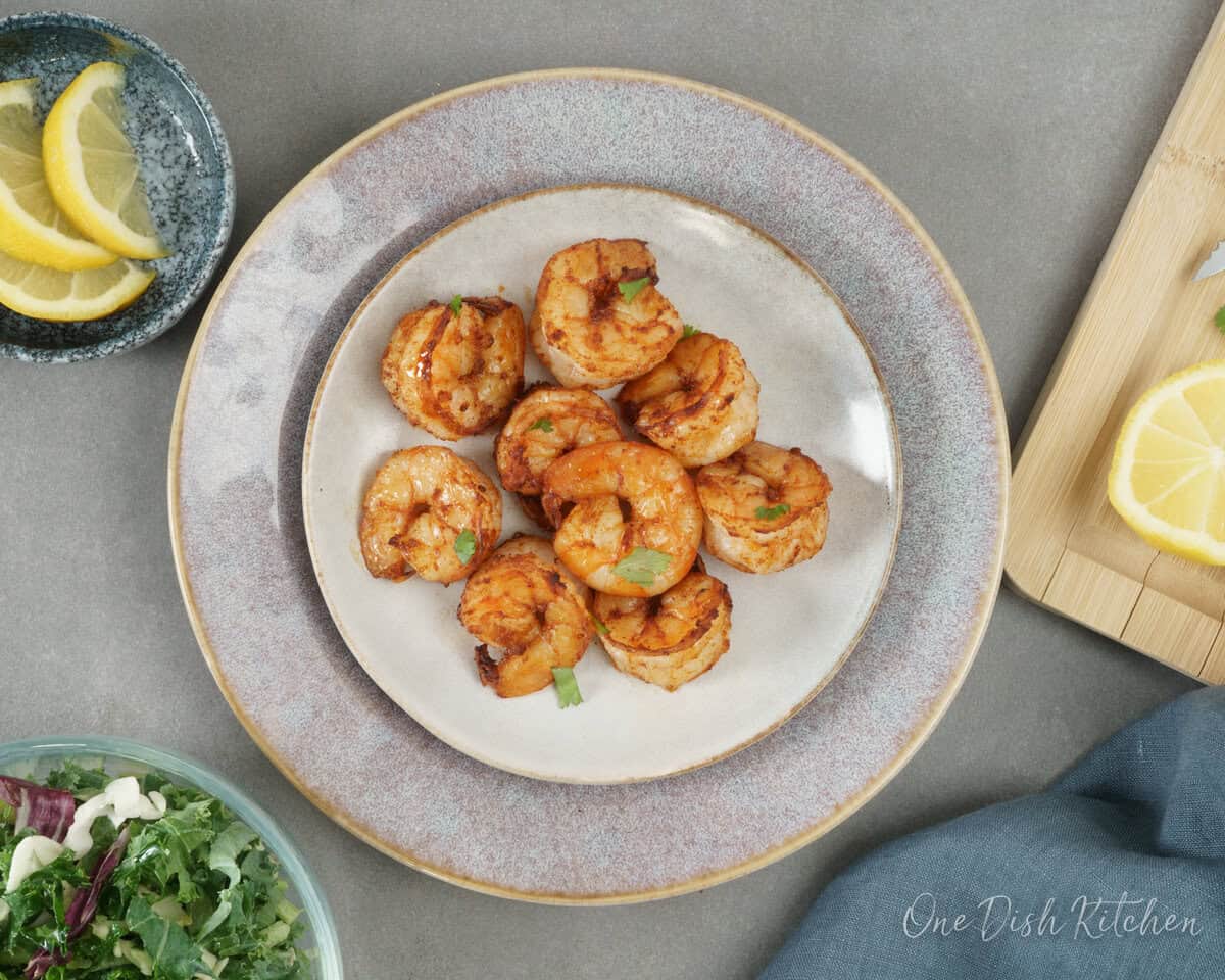 cooked shrimp on a plate next to slices of a lemon and a small salad.
