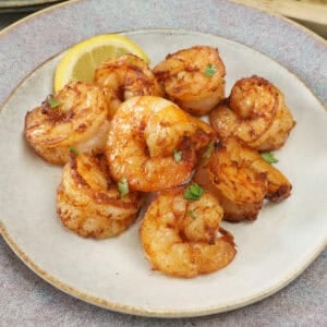 cooked shrimp on a grey plate next to a lemon wedge and a fresh salad.