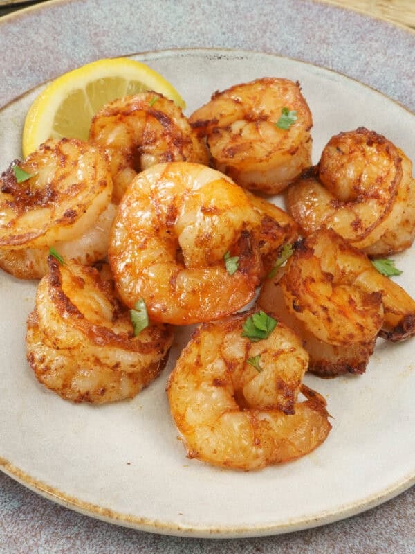 cooked shrimp on a grey plate next to a lemon wedge and a fresh salad.