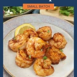 cooked shrimp on a grey plate next to a lemon wedge and a fresh salad.