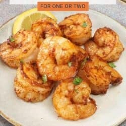 cooked shrimp on a grey plate next to a lemon wedge and a fresh salad.