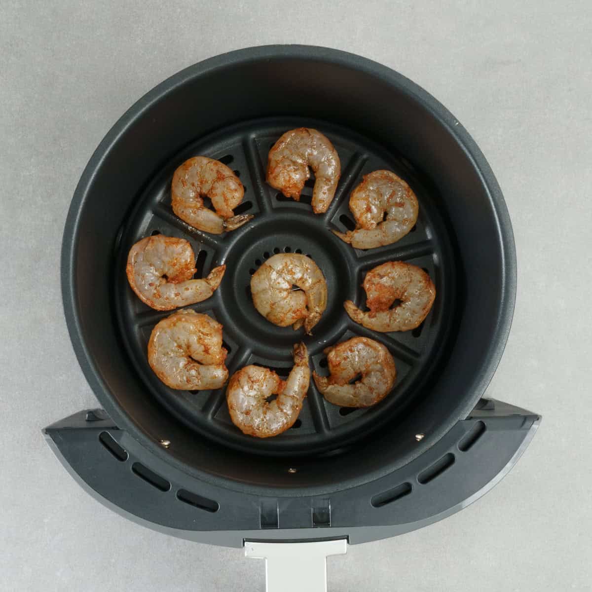 seasoned shrimp in an air fryer basket.