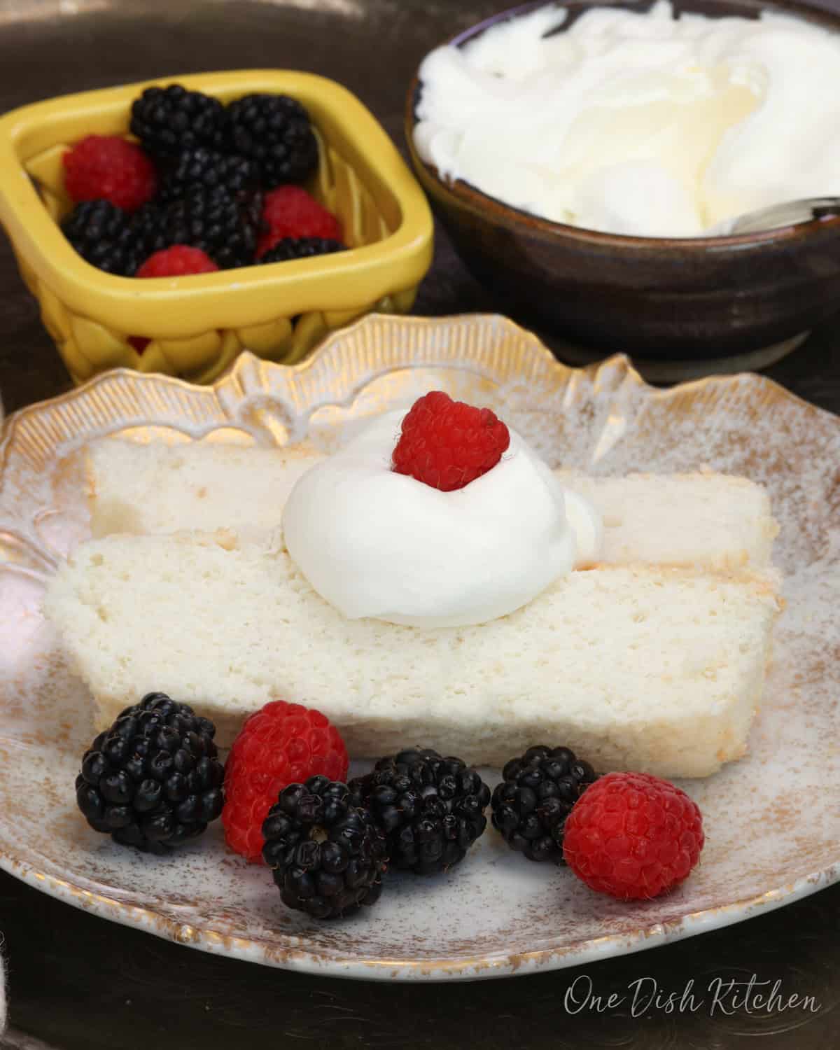 two slices of angel food cake on a white plate topped with whipped cream and surrounded by berries.