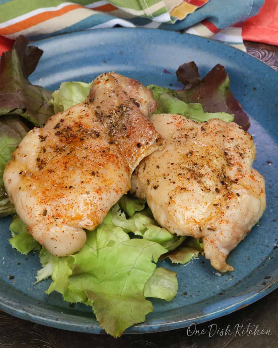 two baked boneless skinless chicken thighs on a bed of lettuce on a blue plate.