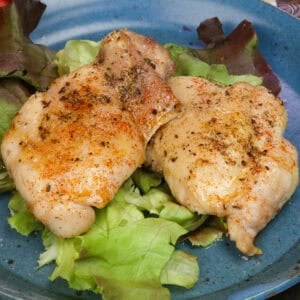 two oven baked boneless skinless chicken thighs on a bed of lettuce.