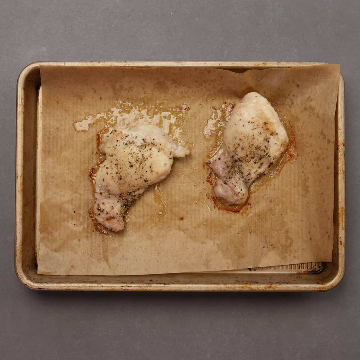 two cooked boneless skinless chicken thighs on a baking sheet.