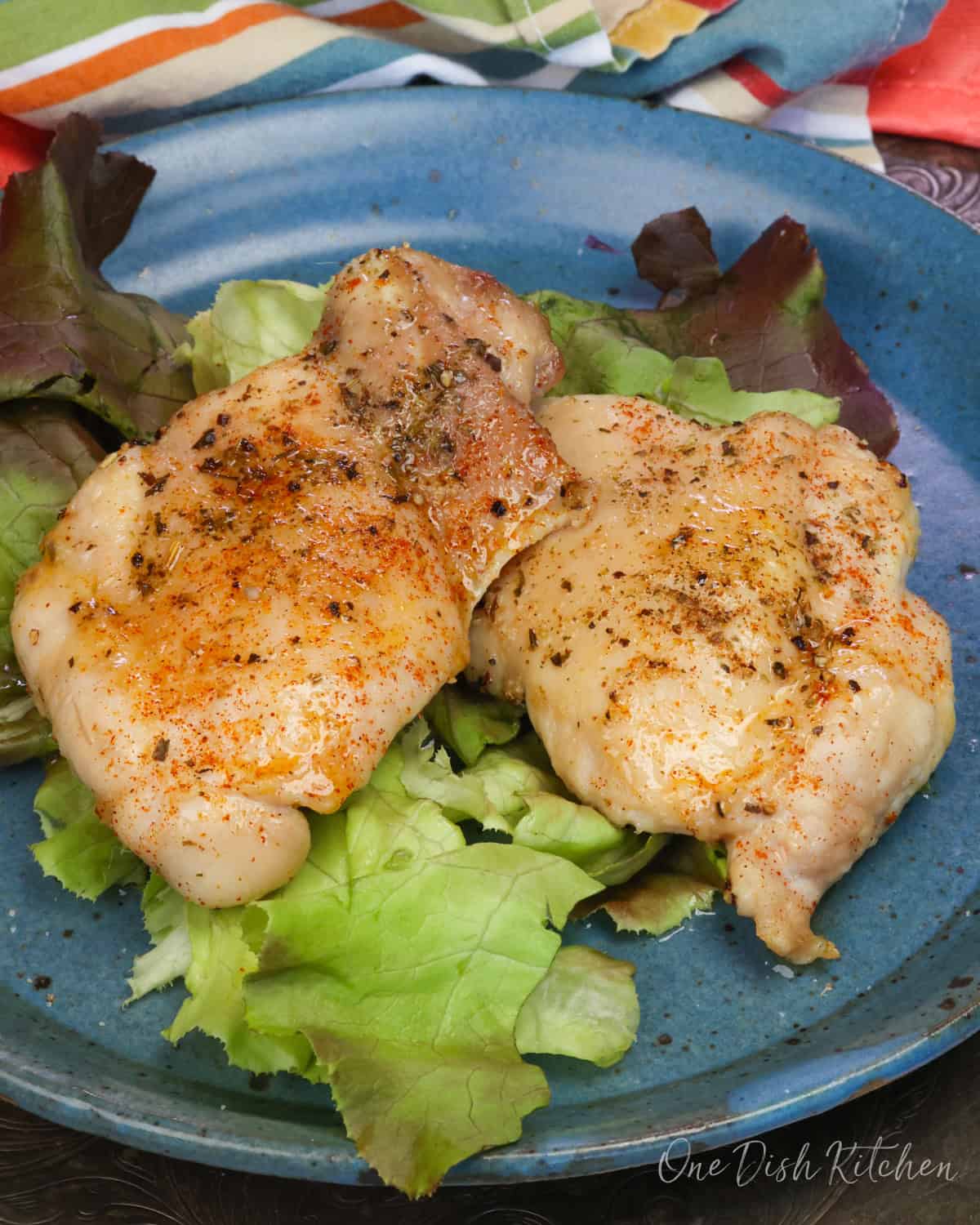 two baked boneless skinless chicken thighs on a bed of lettuce on a blue plate.