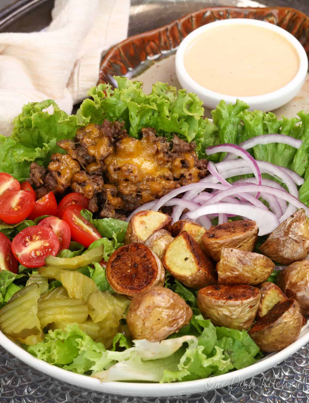 a burger bowl on a silver tray with a bowl of burger sauce on the side.